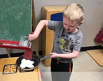 Child playing with toy kitchen, flipping toy food in a pan