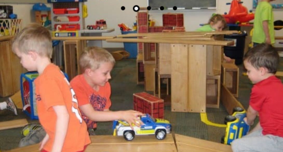 Children playing with toy cars and wooden blocks in a classroom