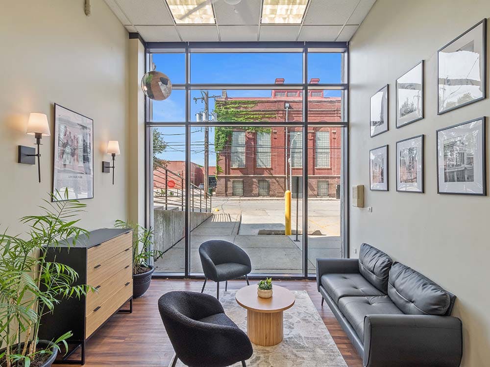 Modern waiting area with sofa, chairs, plants, and a large window facing a building