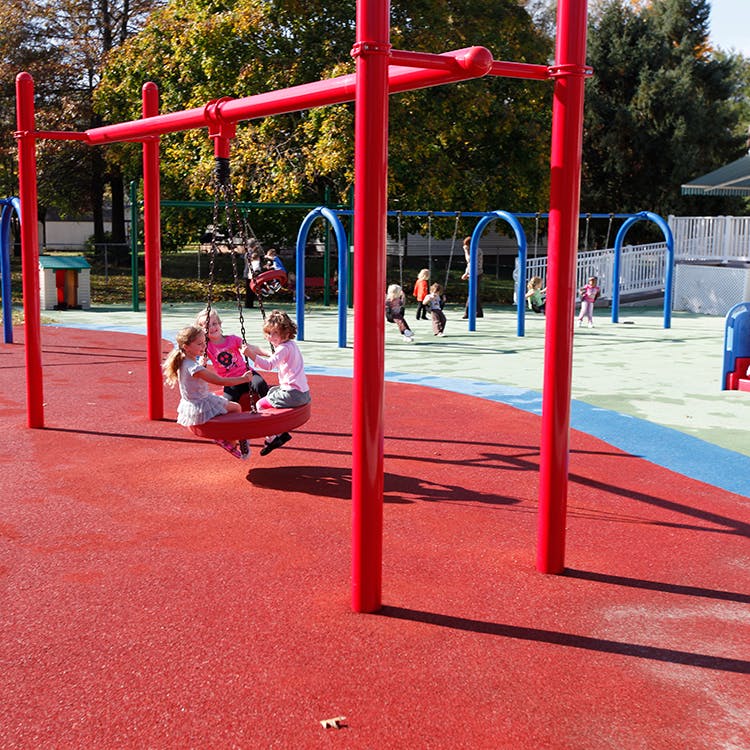 Three children on a red swing at a playground