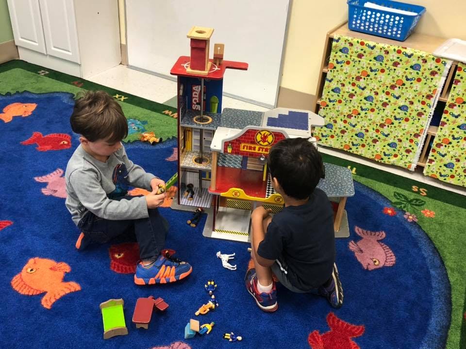 Two children playing with a toy fire station on a blue rug