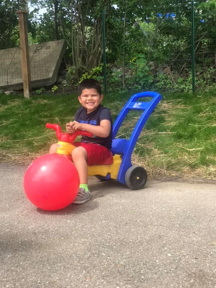 Child sitting on a toy lawnmower with a red ball in front
