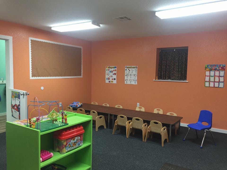 Classroom with small tables and chairs, a green shelf, and orange walls