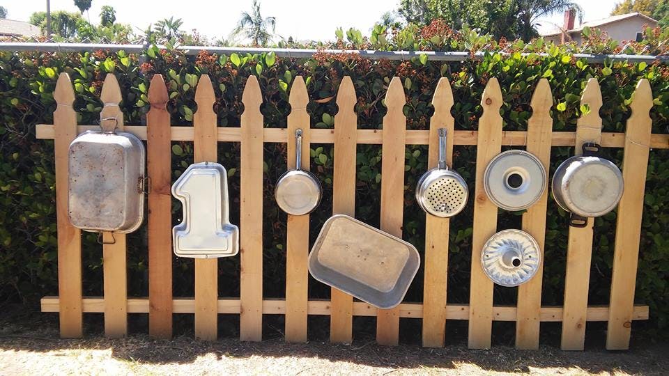 Baking pans and kitchen utensils hanging on a wooden fence