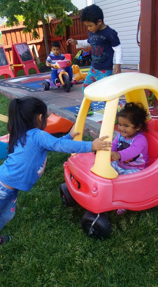 Three children playing with ride-on toys in a yard