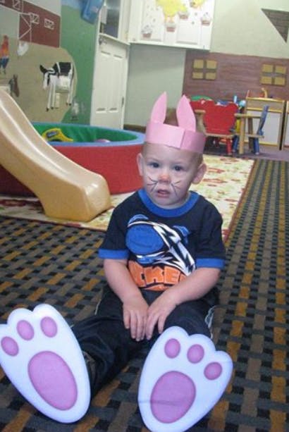 Child in a bunny costume with face paint, sitting on the floor in a classroom
