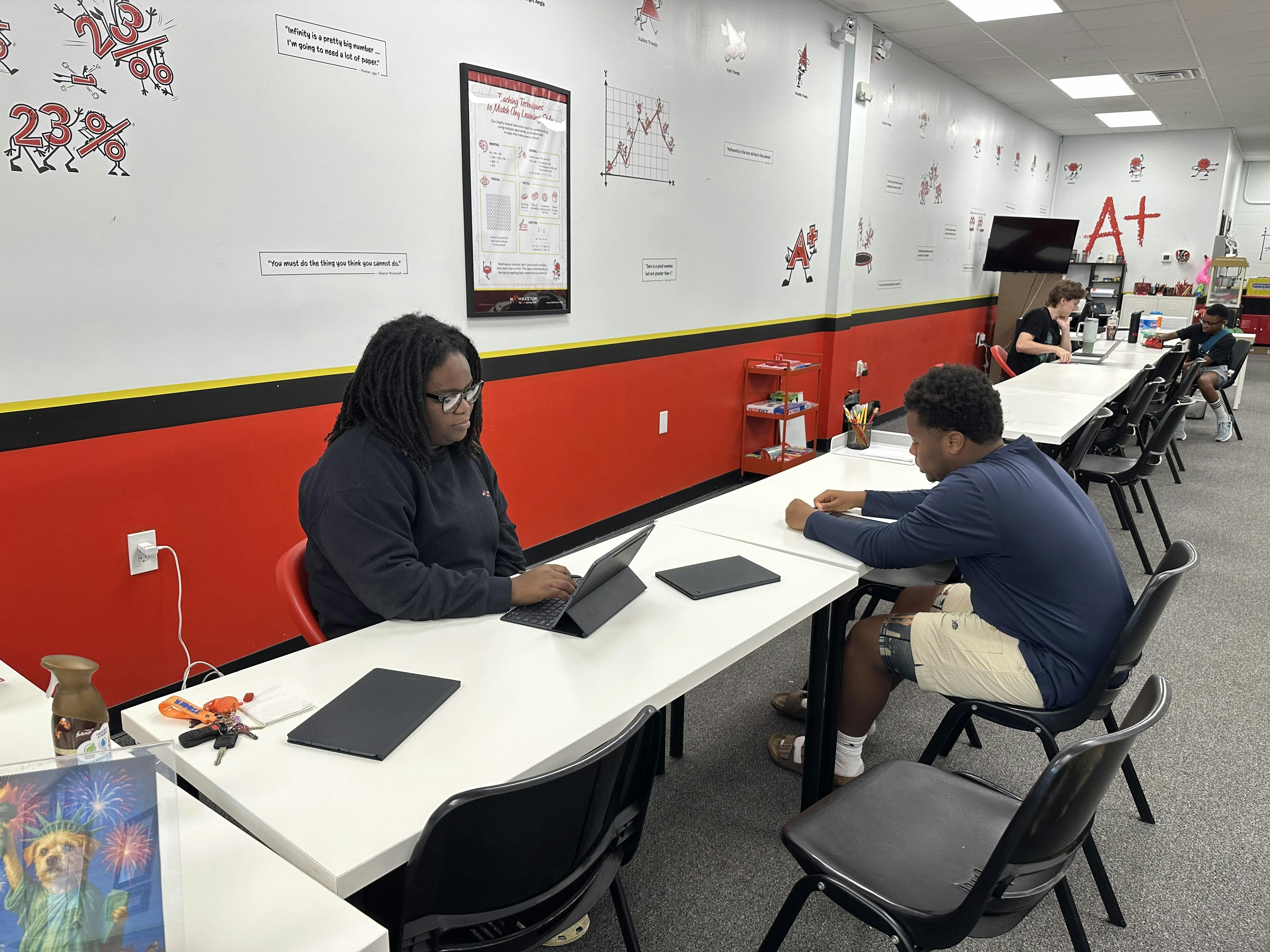 Person typing on a tablet at a long table with another person seated nearby