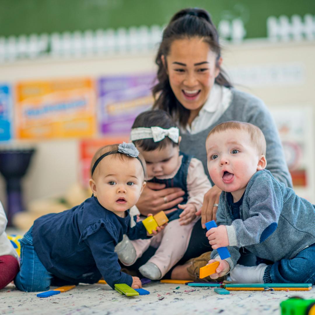 Person with three babies playing with toys on the floor
