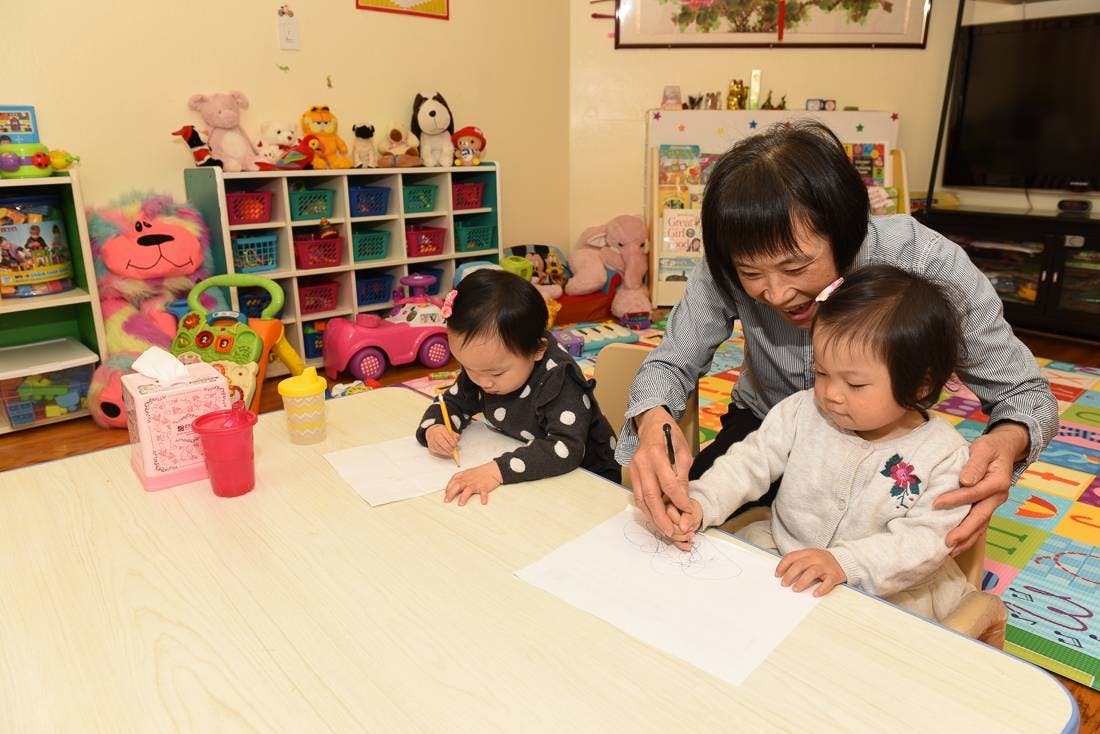 Adult helping a child draw on paper, another child drawing nearby