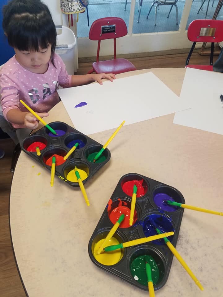 Child painting on paper with a brush and paint tray