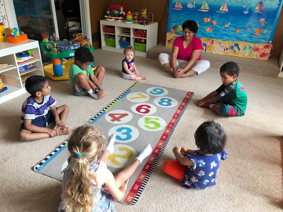 Adult and children sitting on floor around a number mat in a classroom