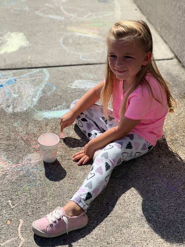 Child sitting on pavement with a cup and chalk drawings