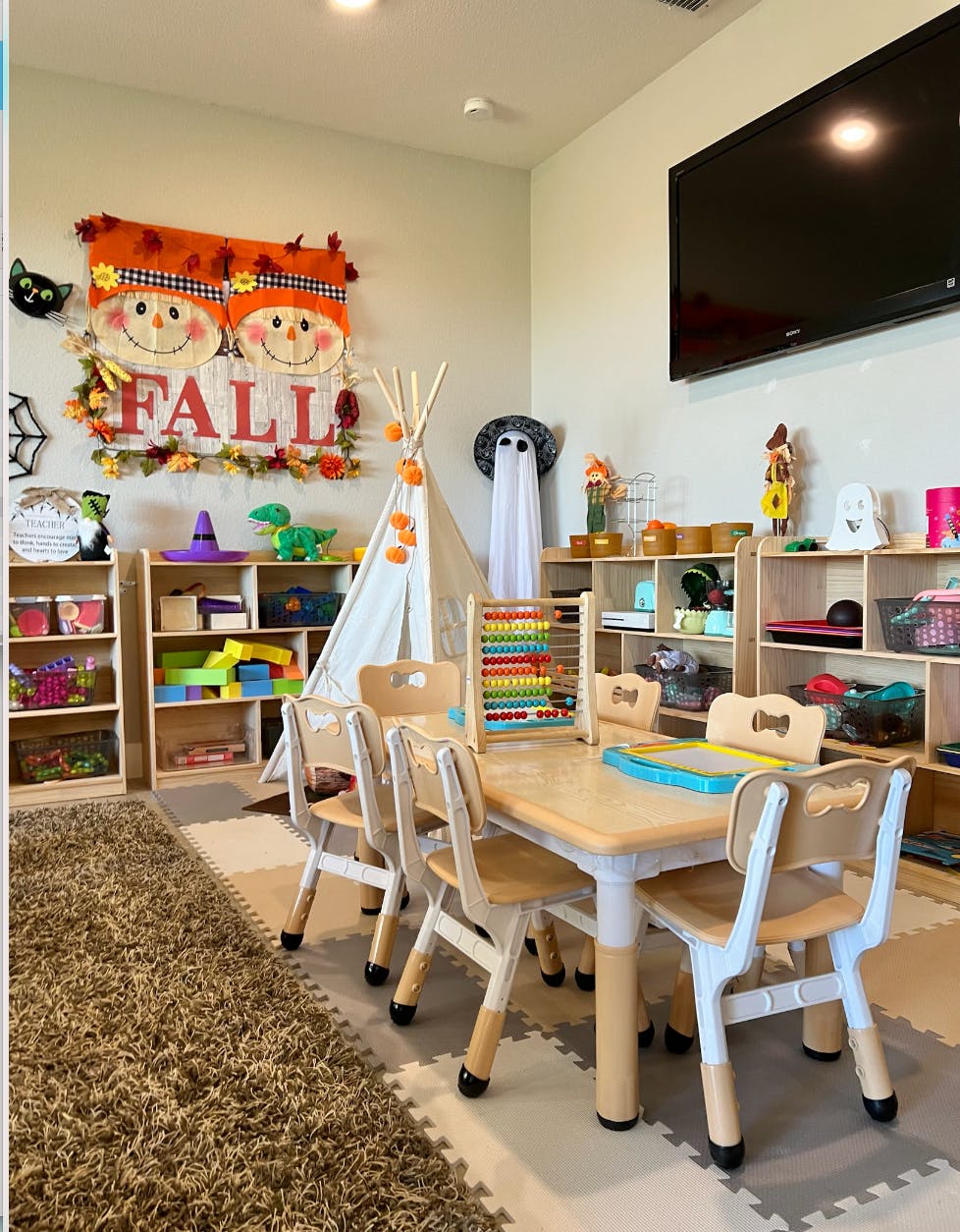 Children's play area with a table and chairs, shelves of toys, and fall decorations