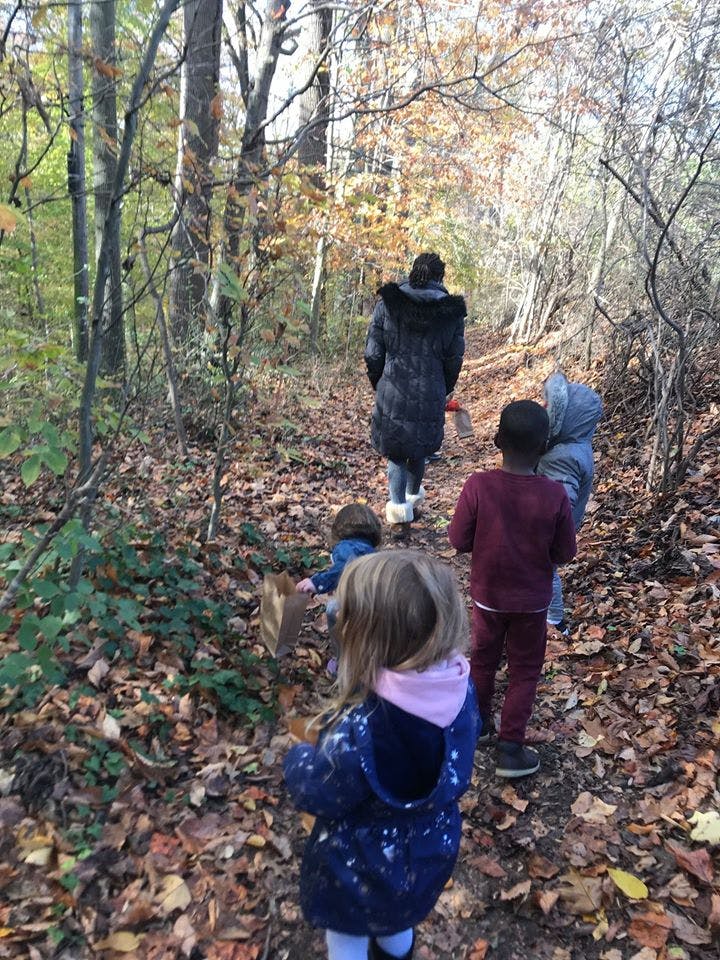 Person and children walking on a leaf-covered path in a wooded area