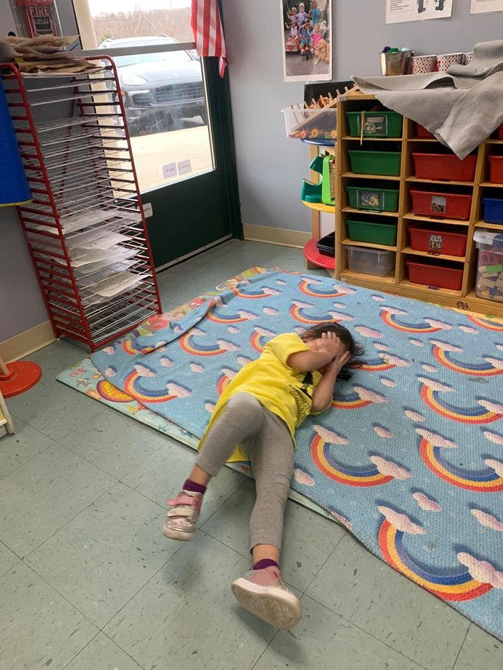 Child lying face down on a rainbow-patterned mat in a classroom