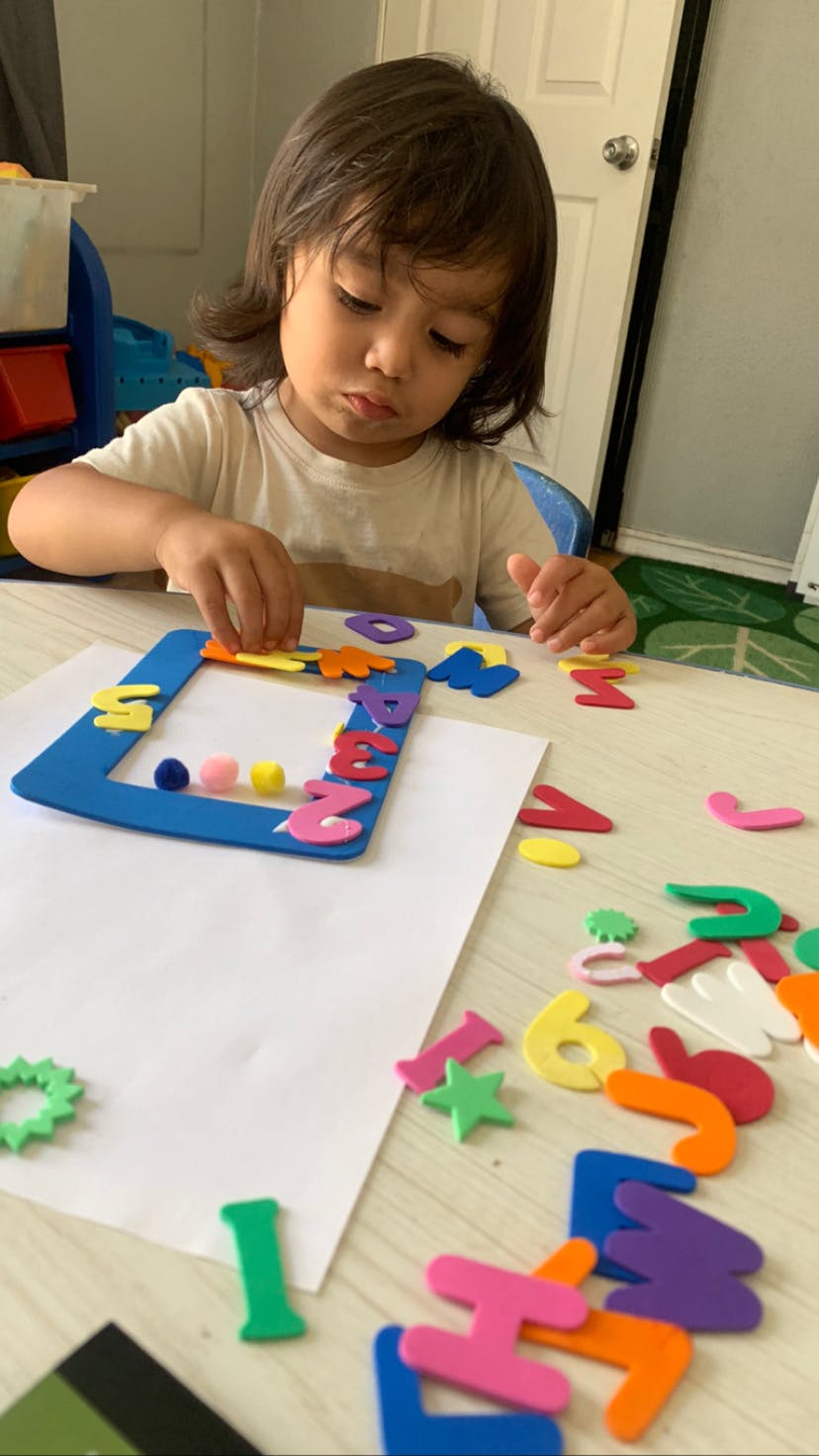 Child playing with colorful foam letters and shapes on a blue frame