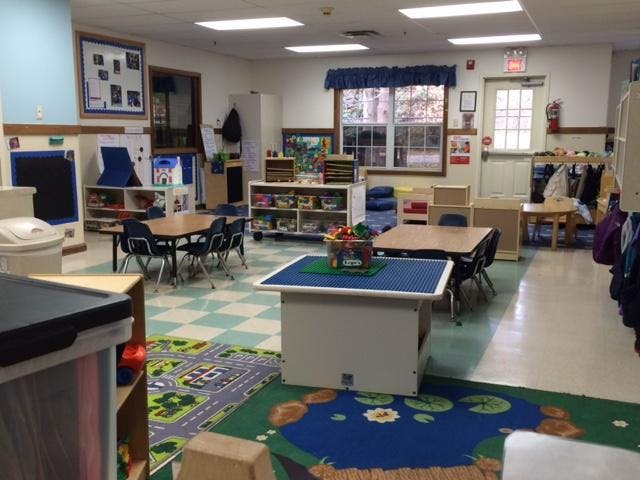 Empty classroom with small tables and chairs, toys, and activity rugs