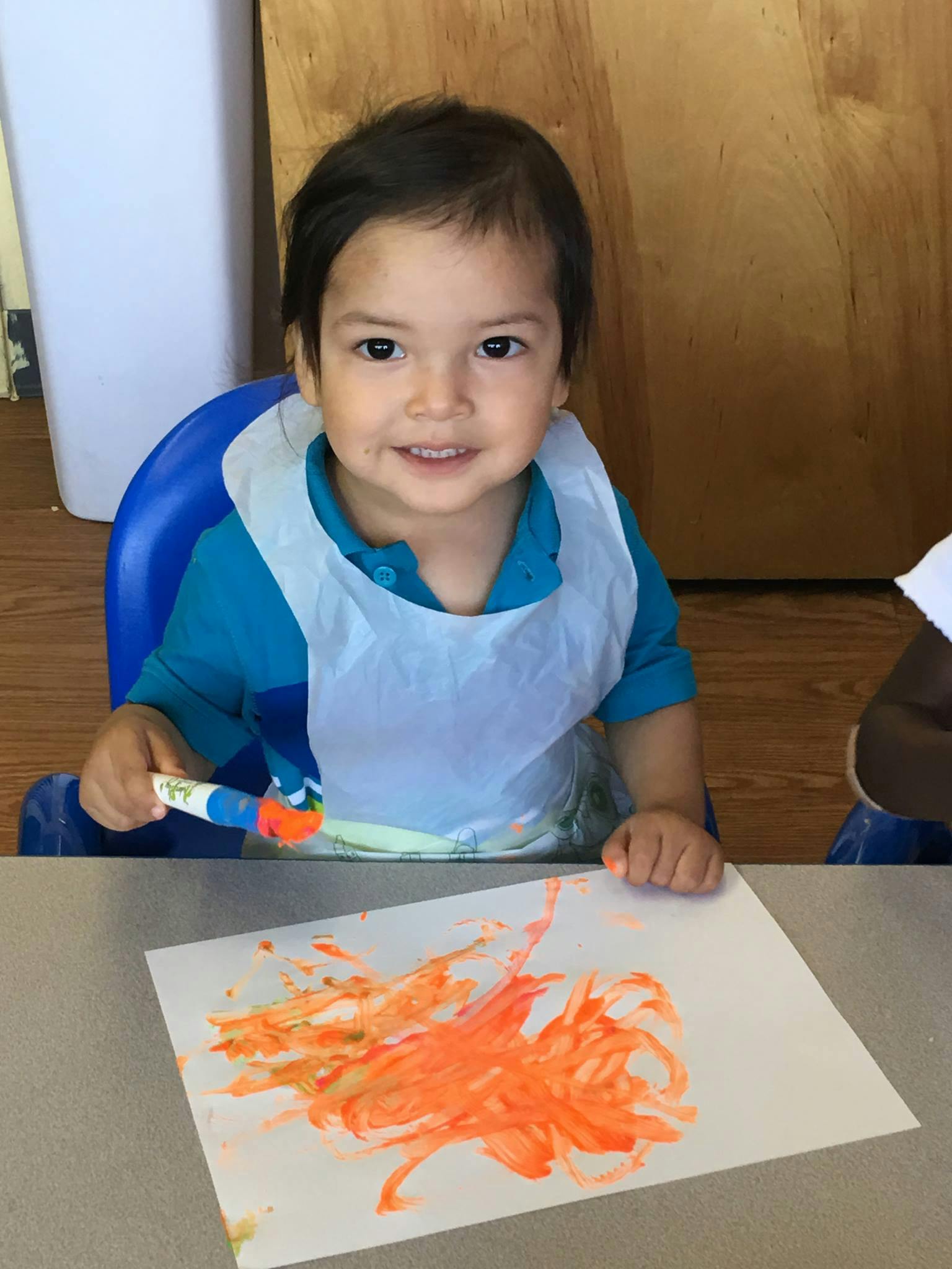 Child in a bib painting with orange paint on paper