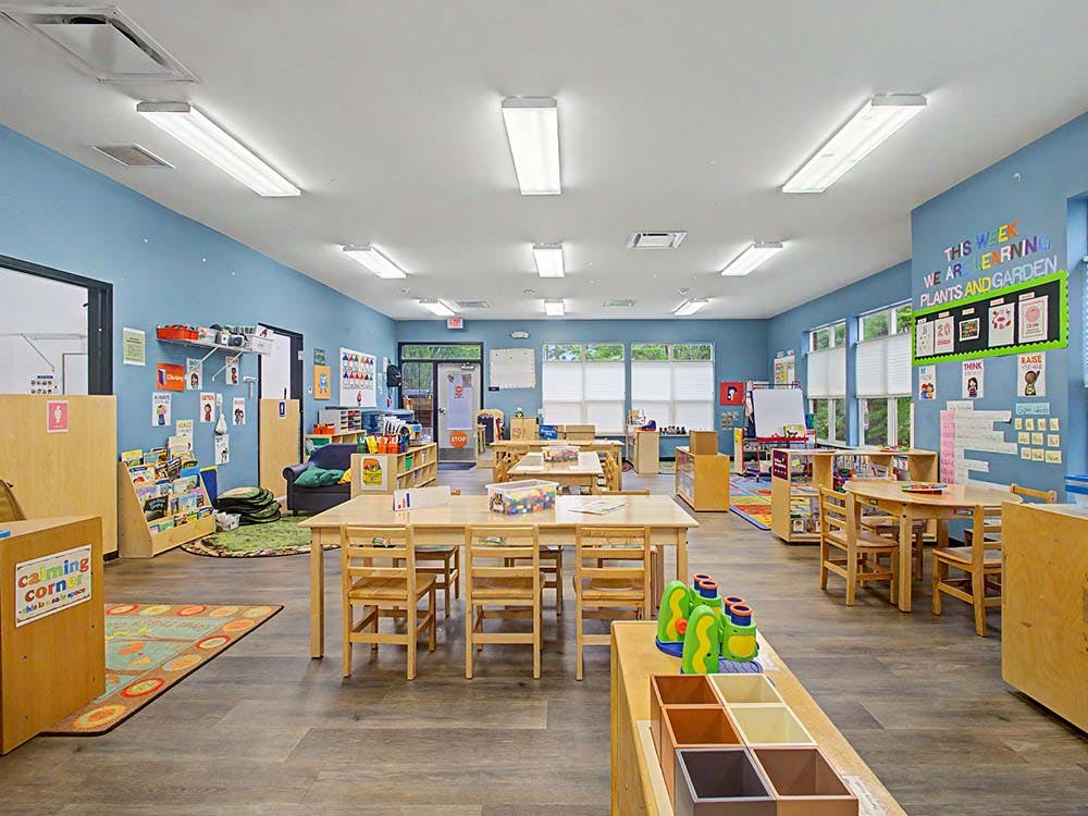 An empty classroom with small wooden tables and chairs, and learning materials