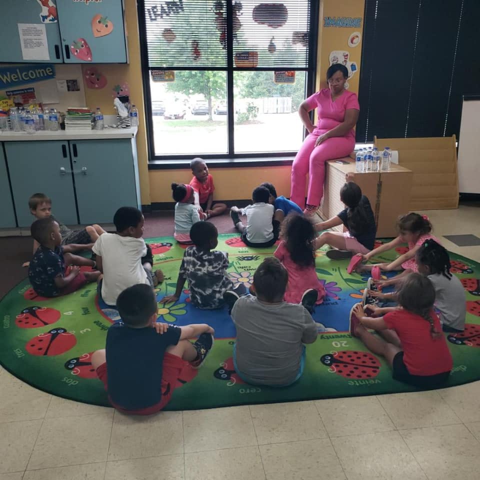 Adult sitting on a table with children sitting on a rug in a classroom