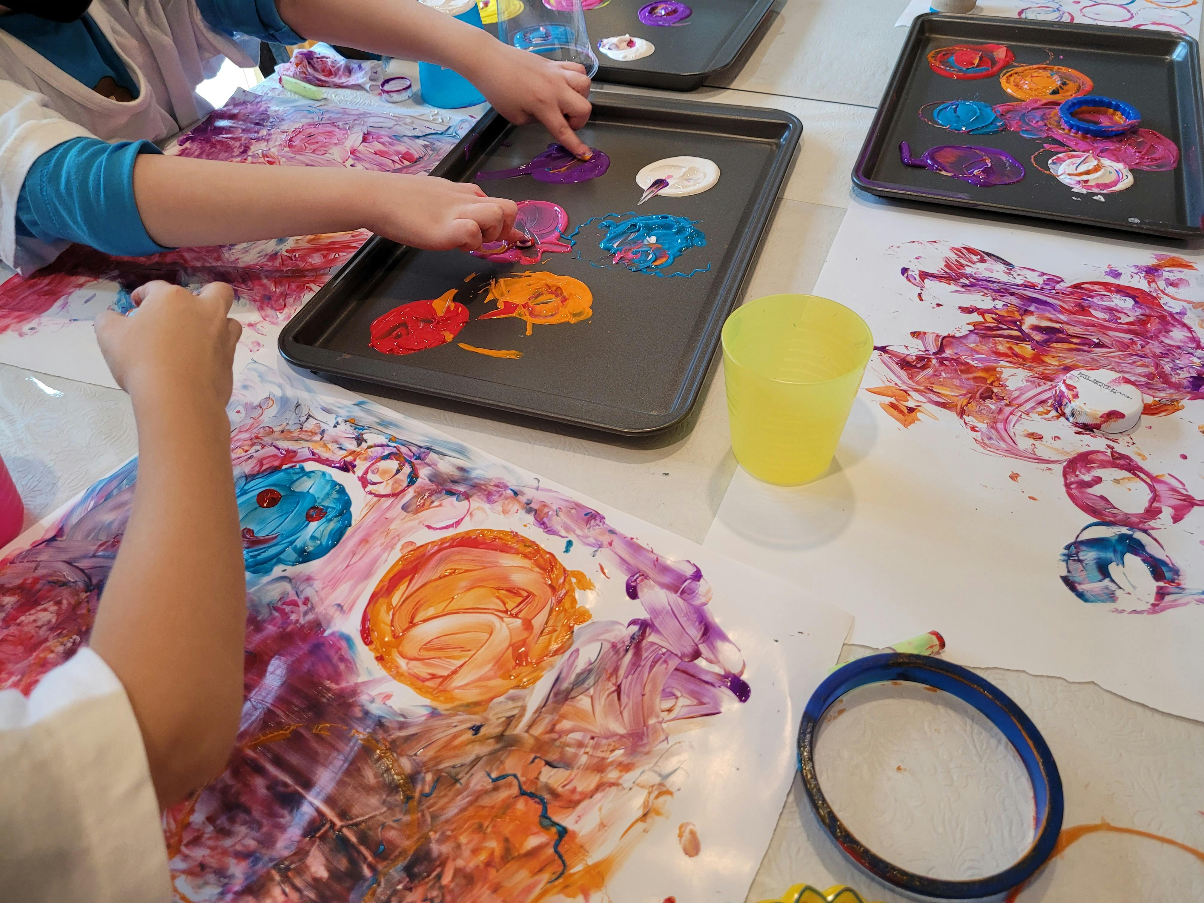 Children finger painting with various colors on paper and trays