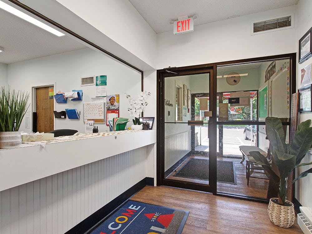 Reception area with a white counter and glass double doors, an exit sign above