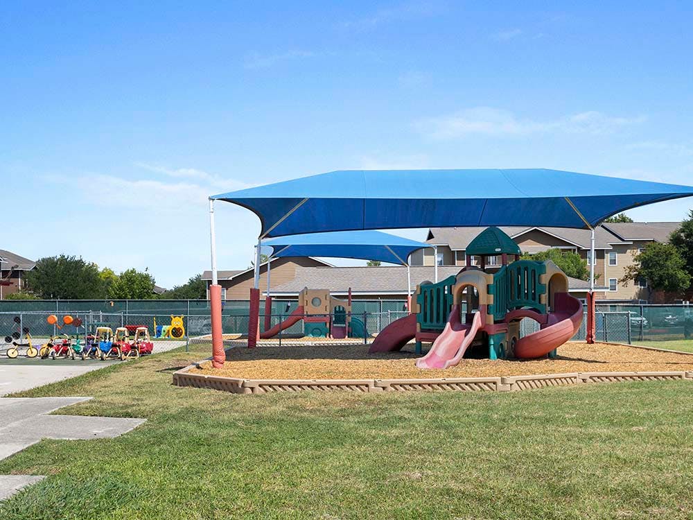 A colorful playground with slides and swings under a blue shade canopy