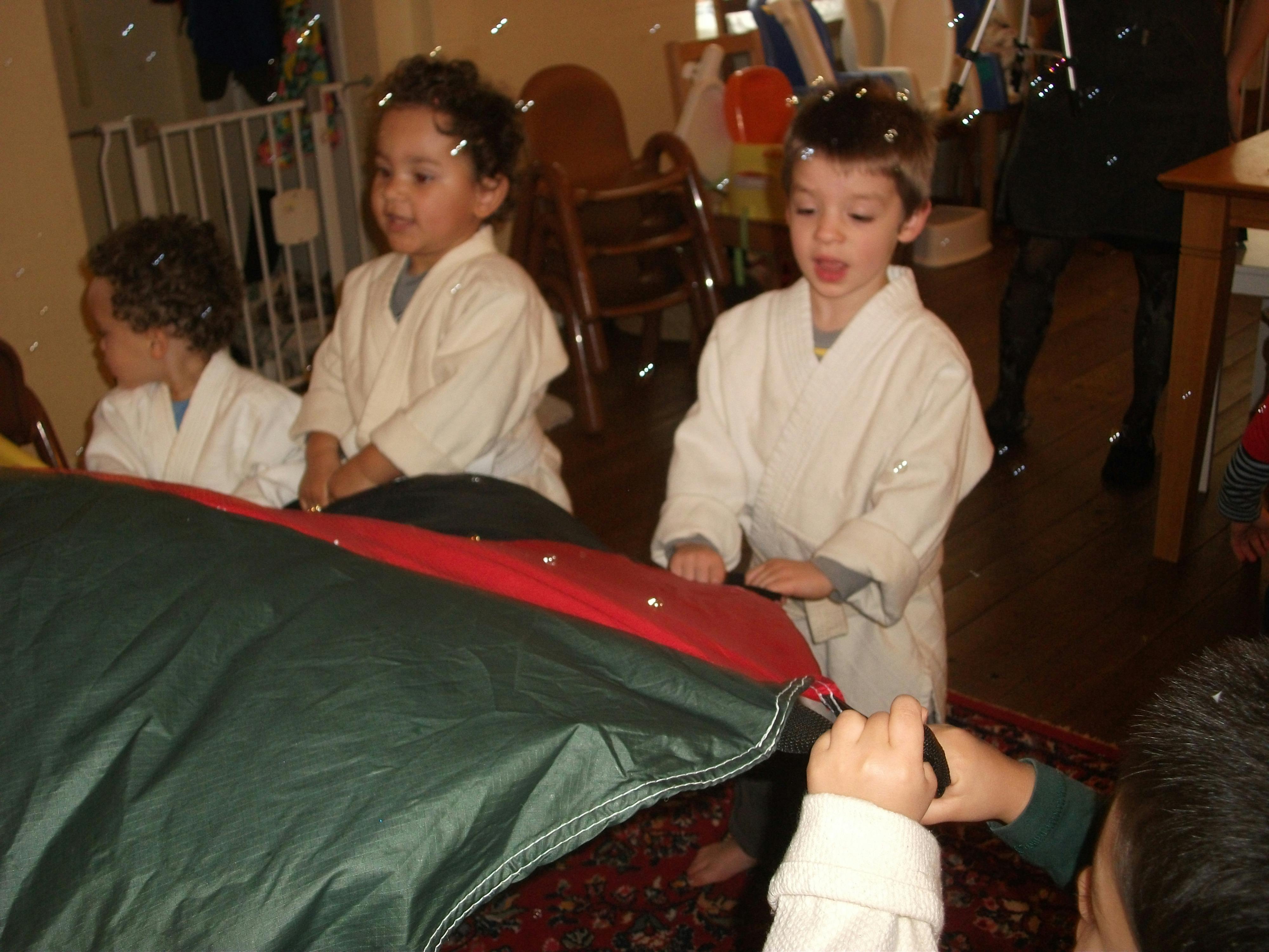 Three children in white robes playing with a red and green parachute