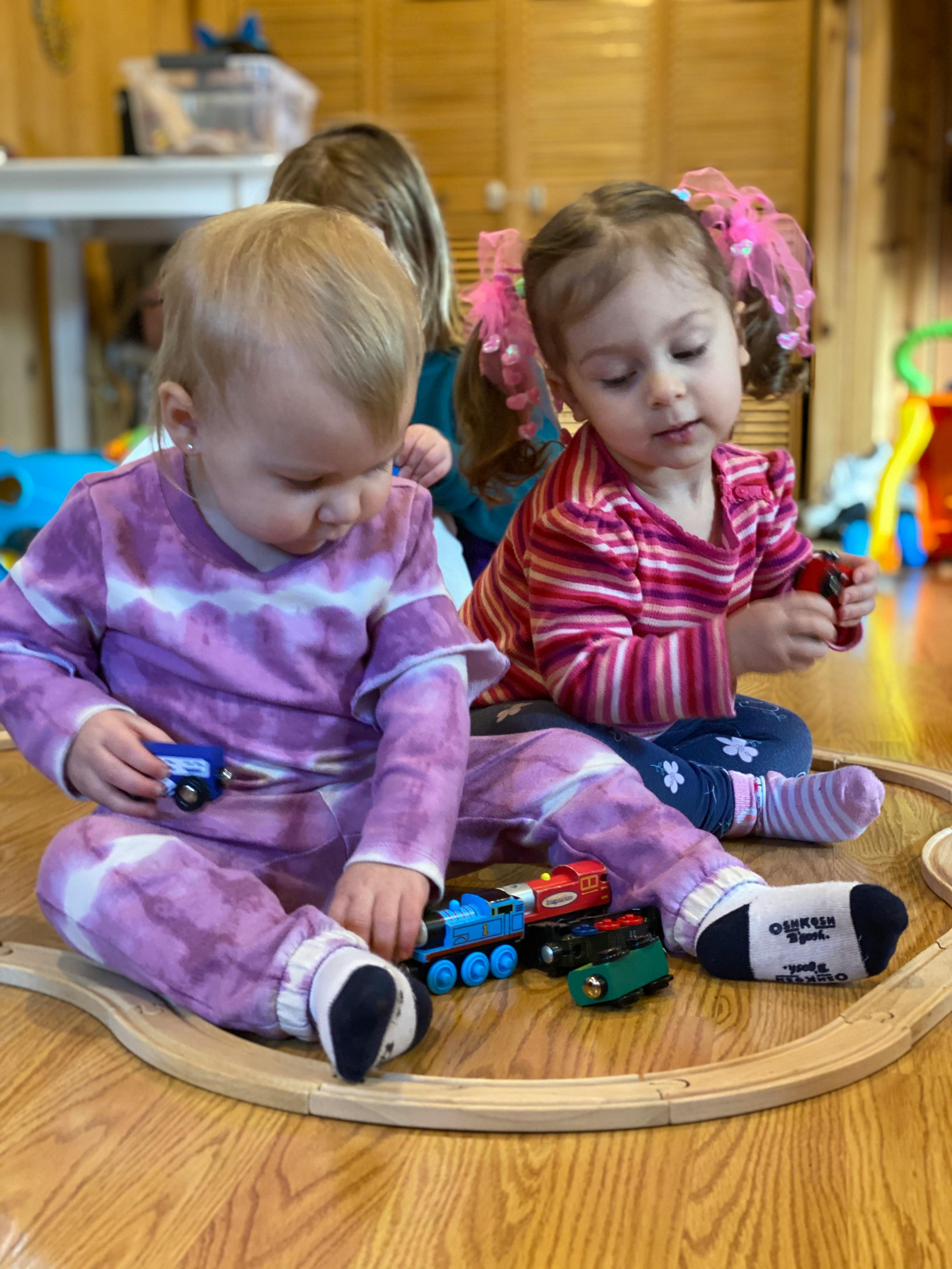 Two children playing with toy trains on a wooden track