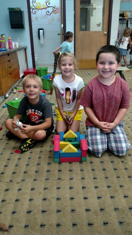 Three children kneeling on a carpet with colorful blocks