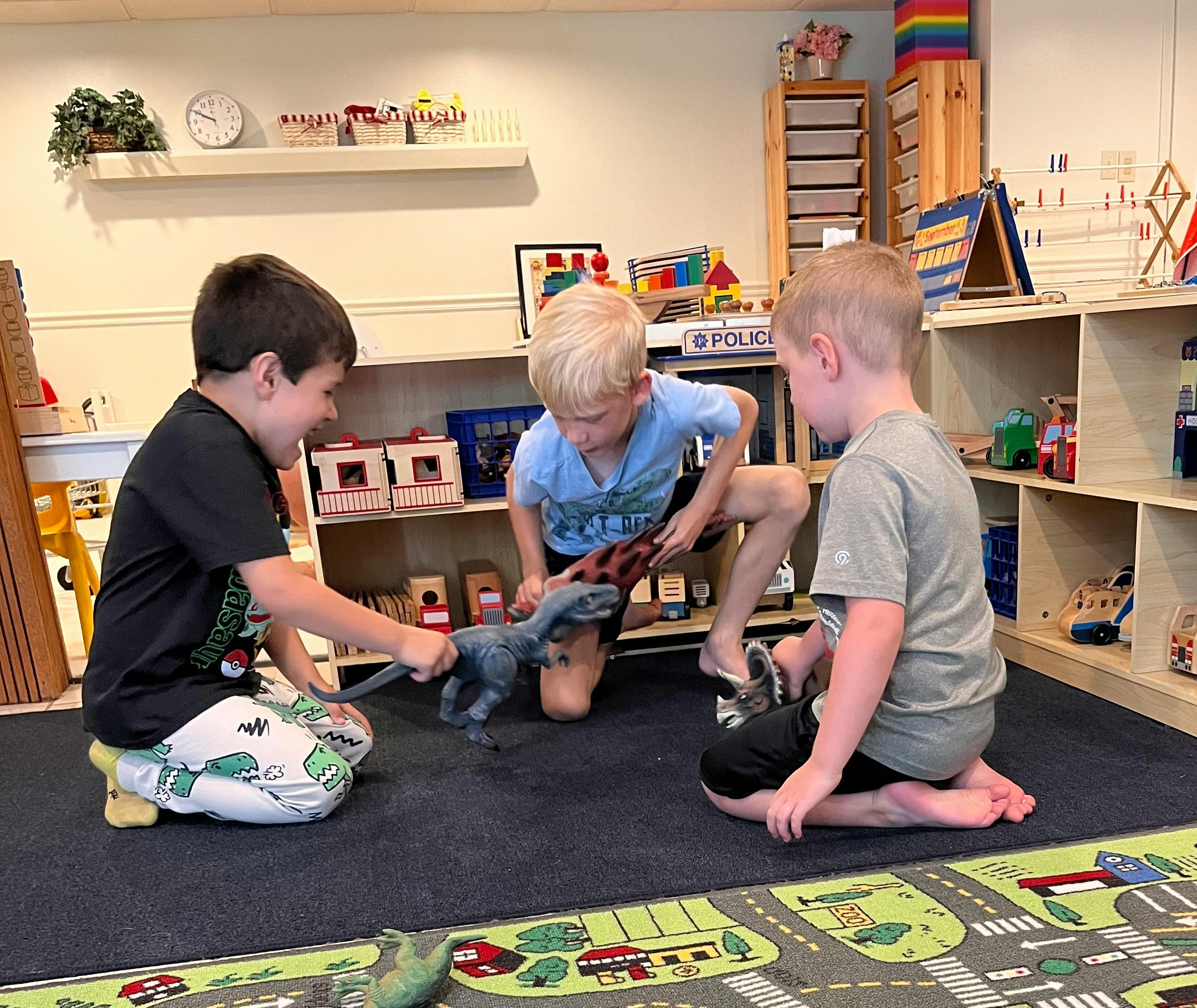 Three children playing with toy dinosaurs on a rug