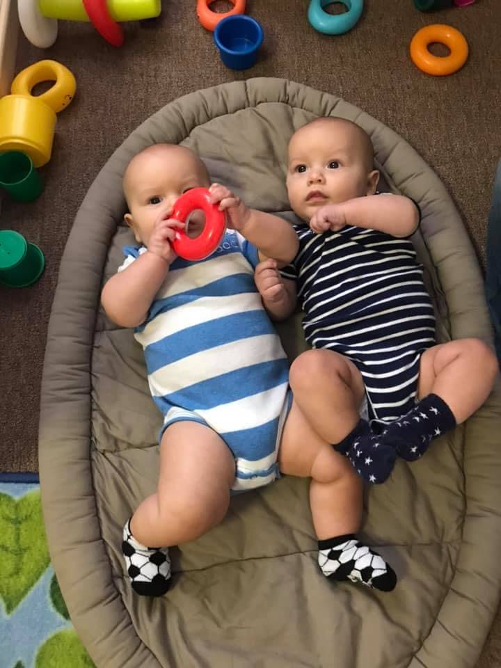 Two babies lying on a mat, one holding a red toy