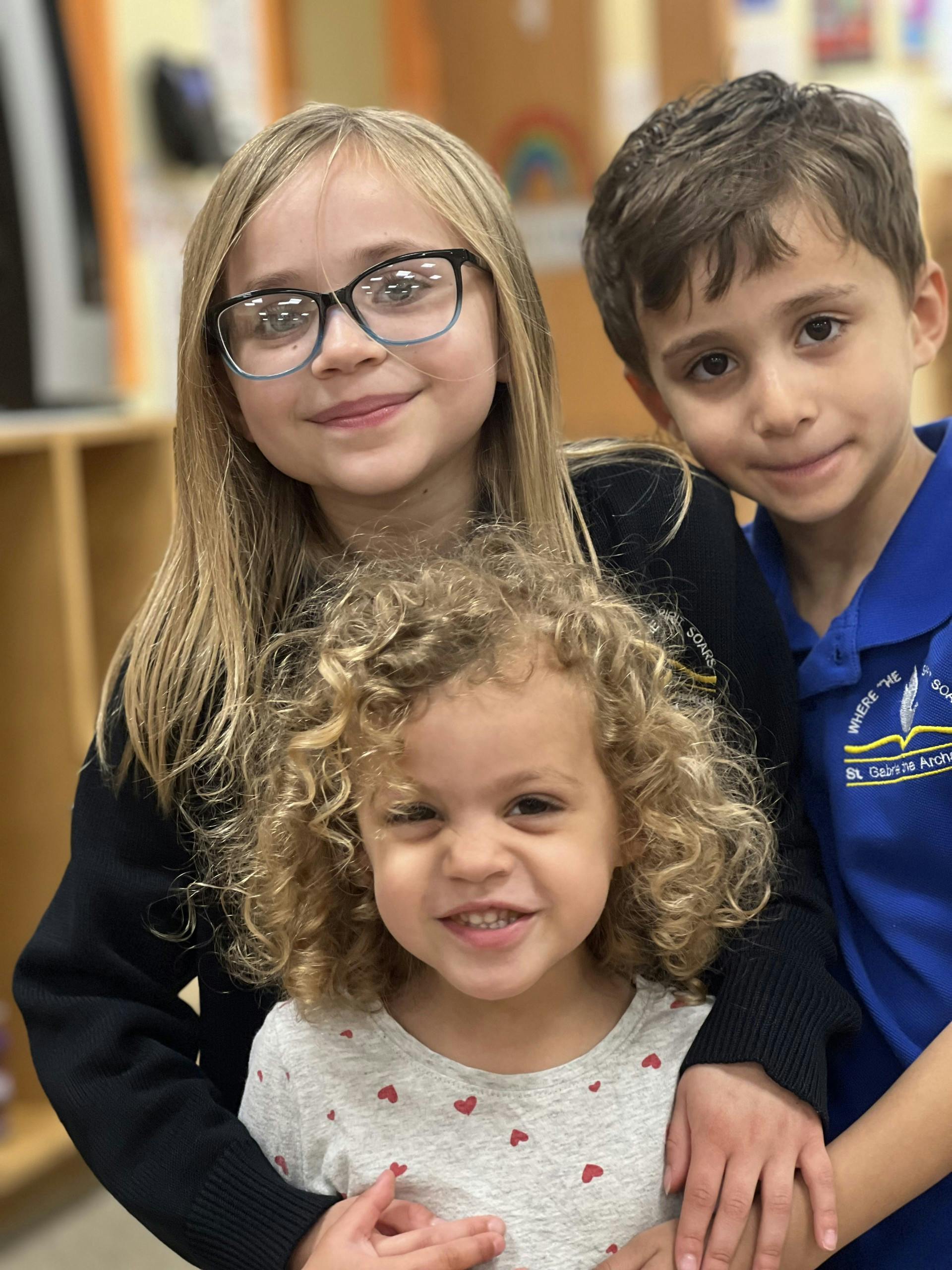Three children posing together, one with glasses, one with curly hair