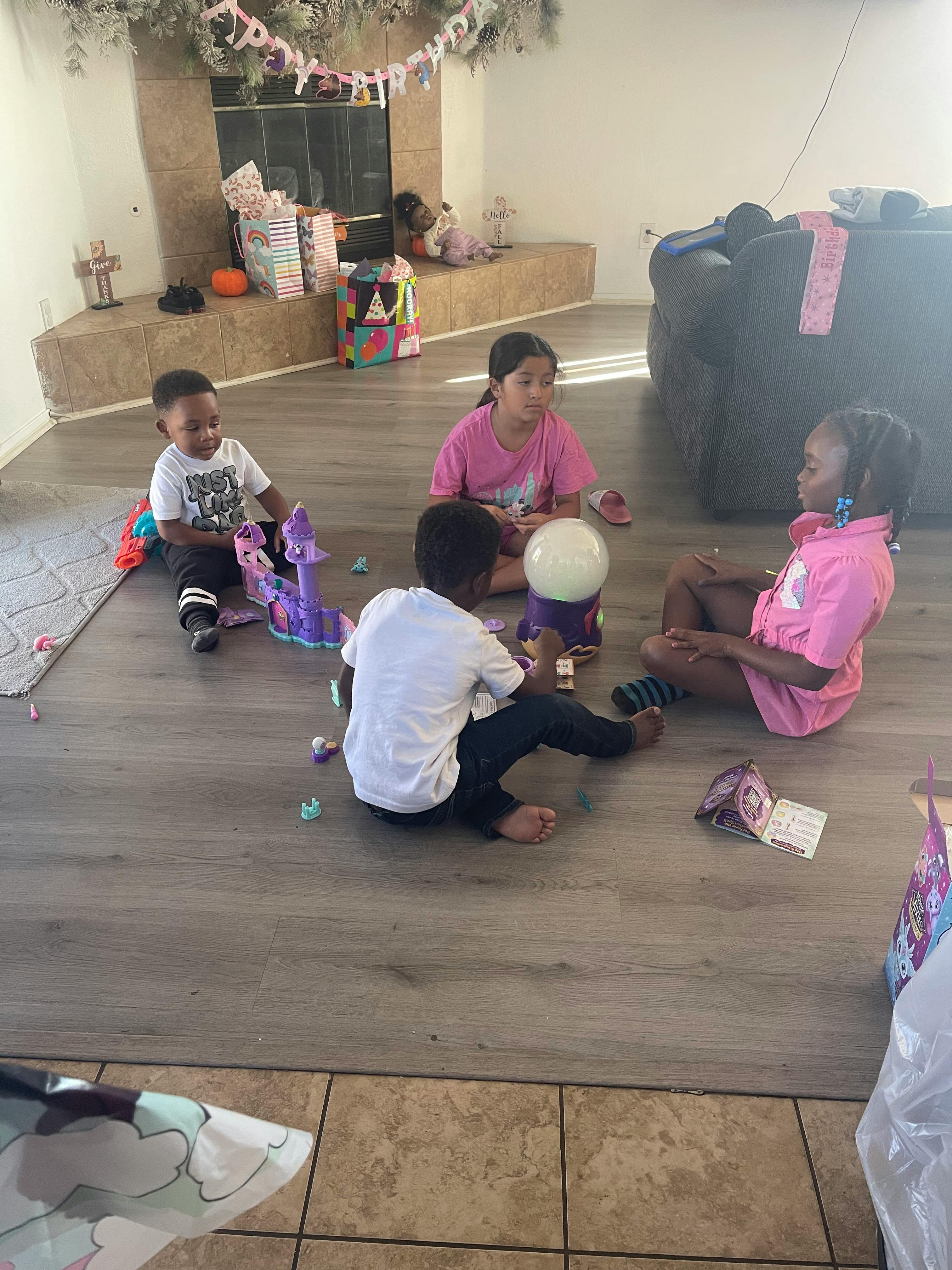 Four children playing on a floor with toys on a wooden floor