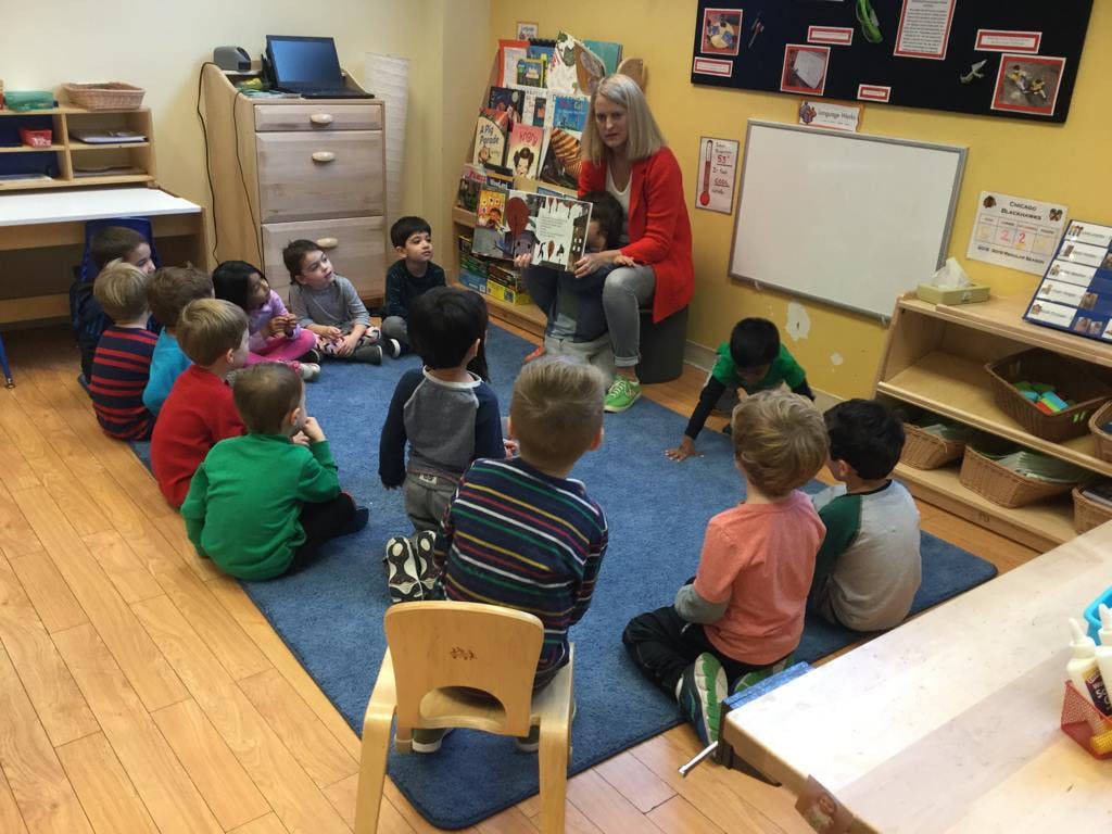 Adult reading a book to a group of children sitting on a rug