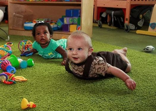 Two babies crawling on a green carpet with toys