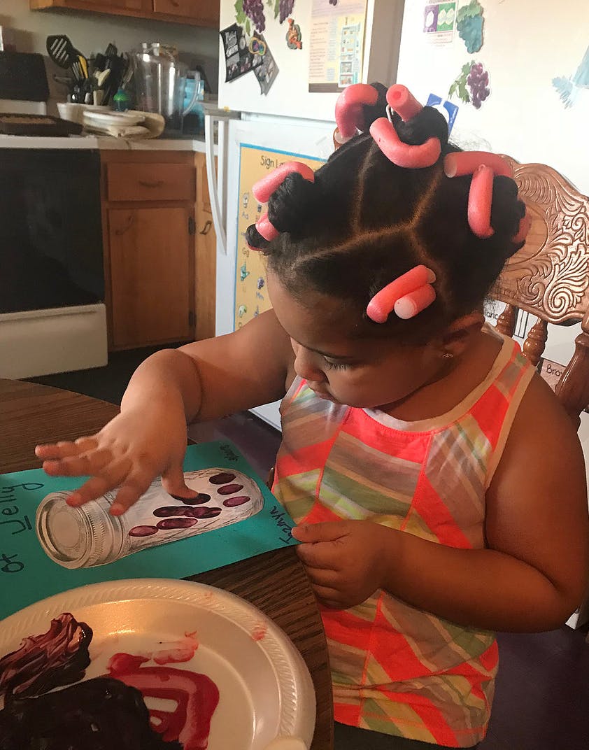 Child with hair curlers touching a drawing of a jar
