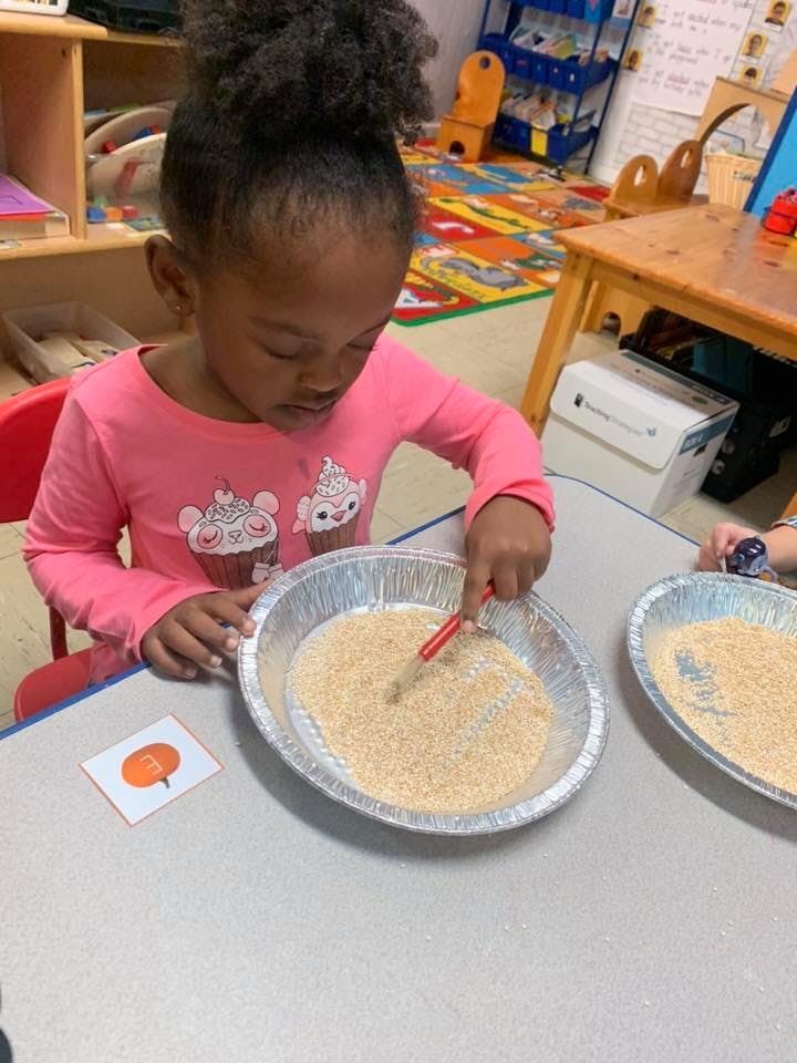 Child drawing in a tray of rice with a stick