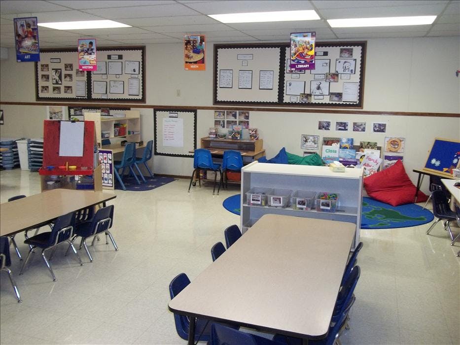 Empty classroom with small tables and chairs, an easel, and display boards