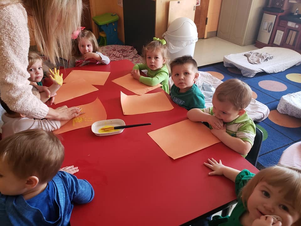 Adult and multiple children at a red table with orange paper and paint