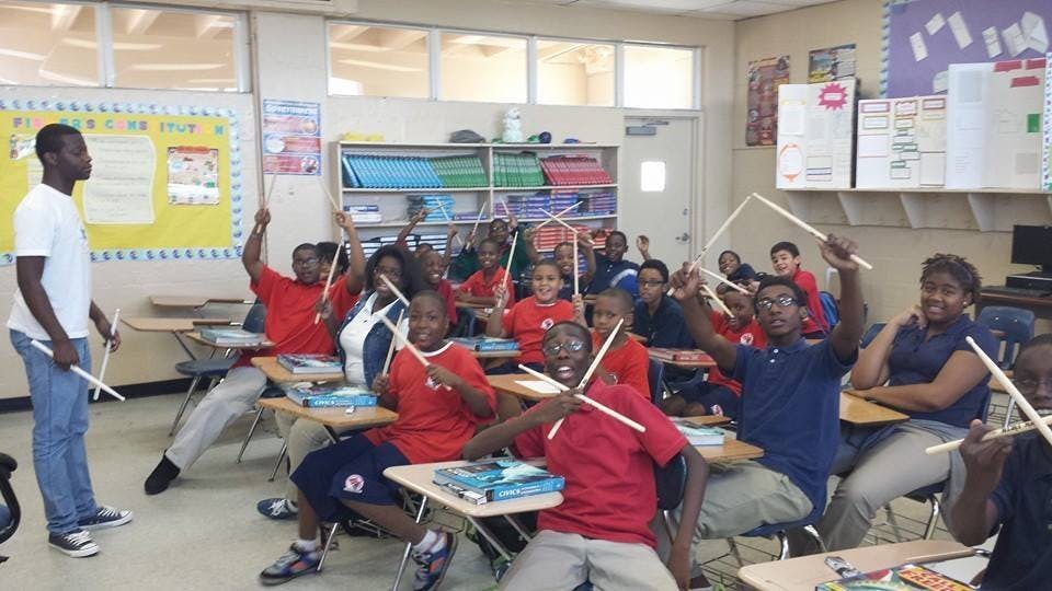 People in a classroom holding drumsticks