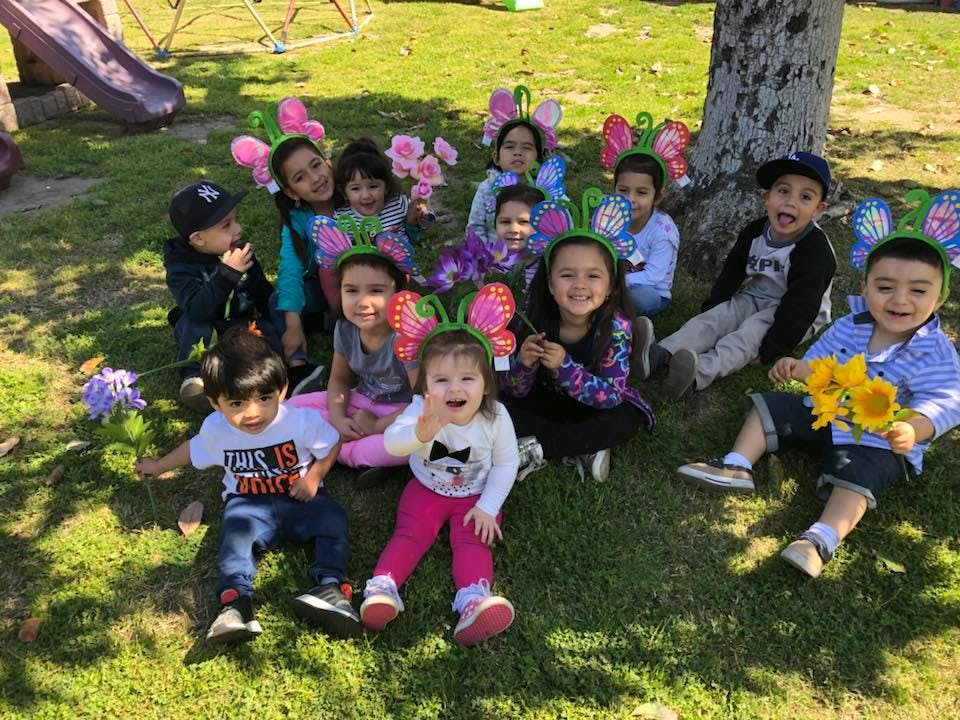 Group of children sitting on grass, some wearing butterfly headbands
