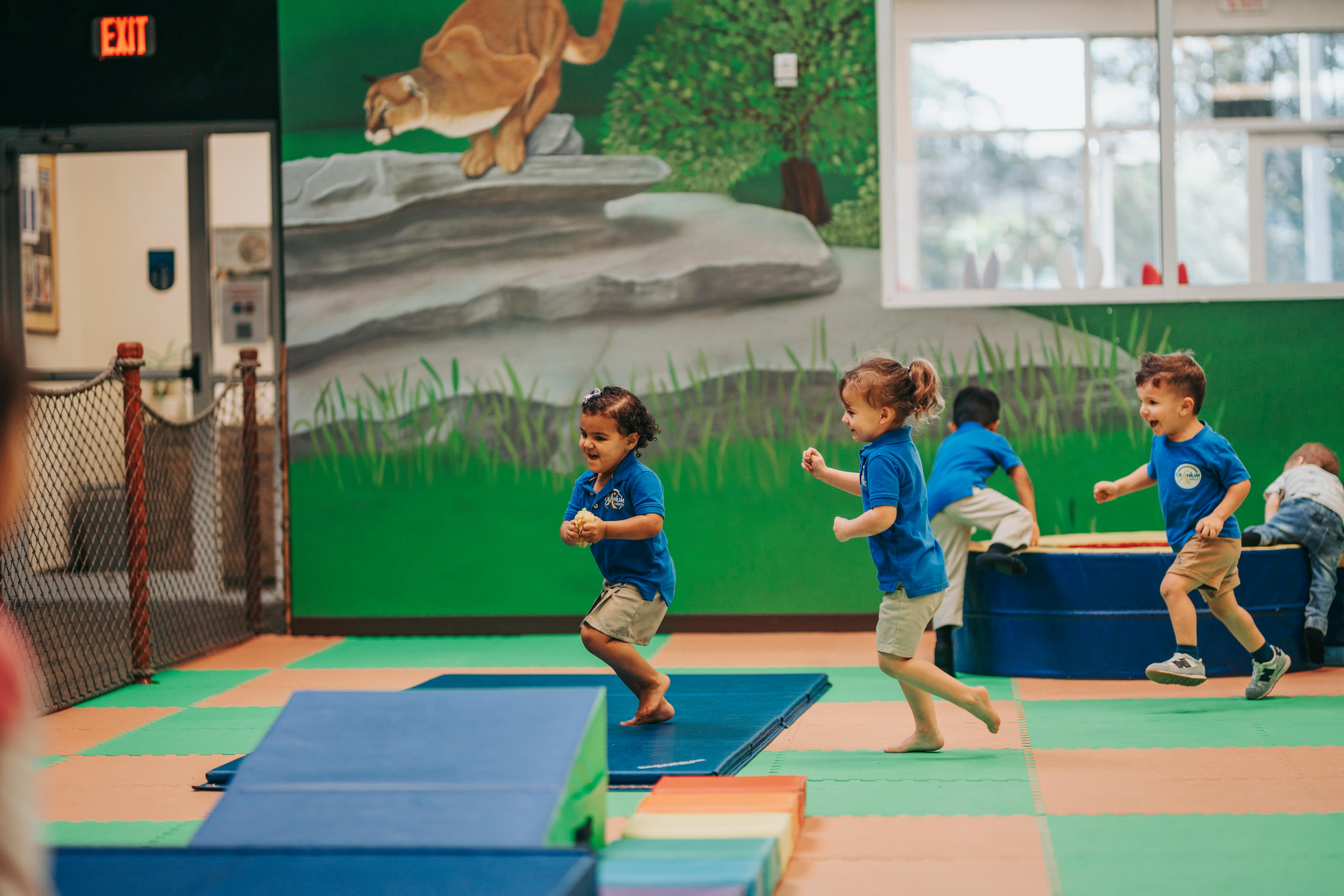 Children running and playing on mats in a room with a mural