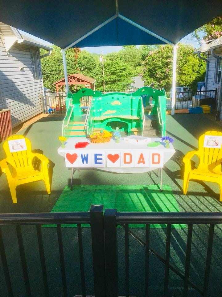 Table with "WE LOVE DAD" banner and two yellow chairs on a playground