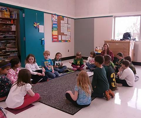 Adult and children sitting in a circle on a rug in a classroom