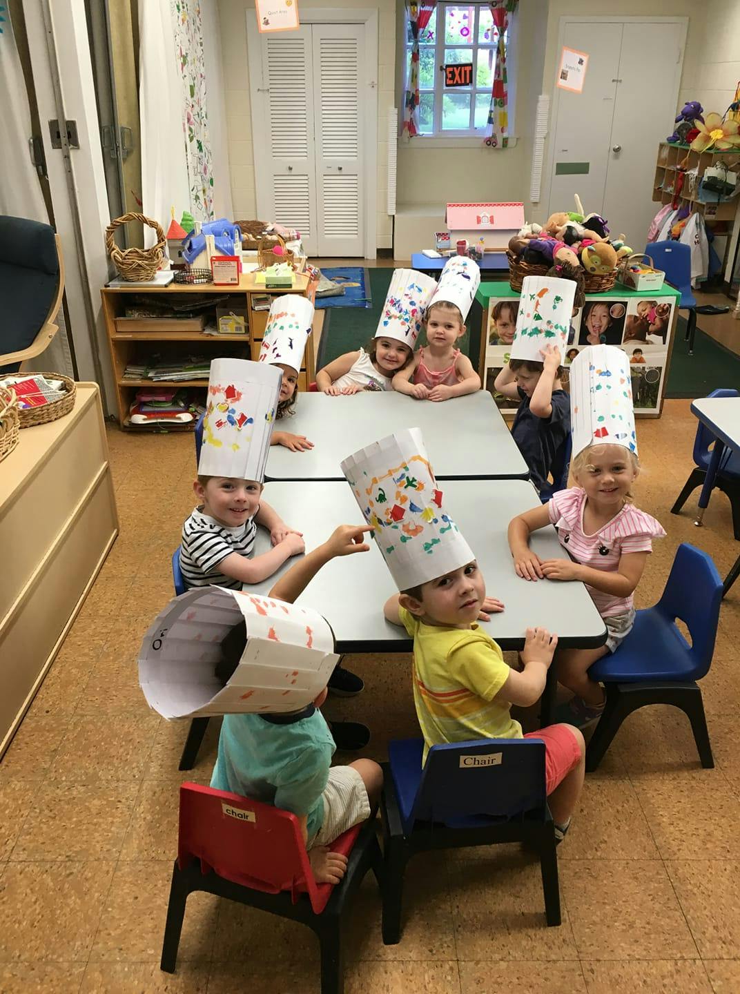 Children wearing paper chef hats sitting at tables in a classroom