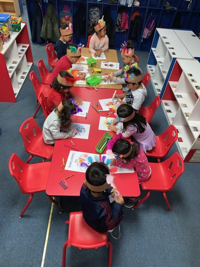 Children sitting at red tables, drawing and coloring in a classroom