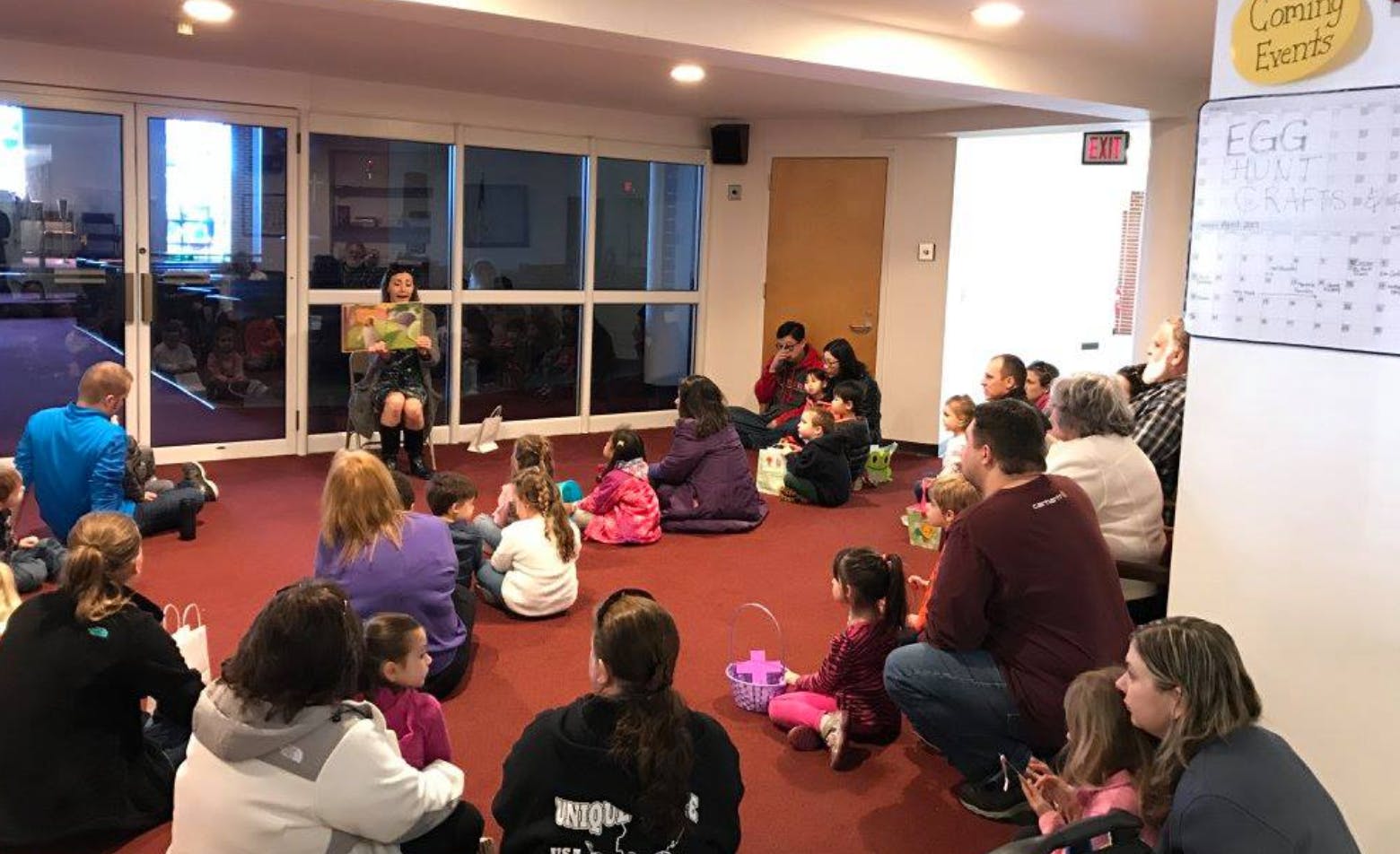 Adult reading to a group of adults and children sitting on the floor