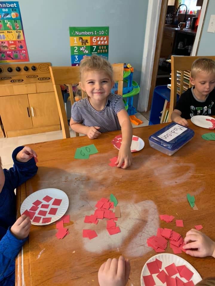 Child at a table with other children, working with red paper cutouts