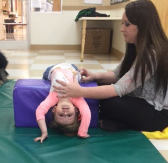 Person assisting a child hanging upside down over a purple block